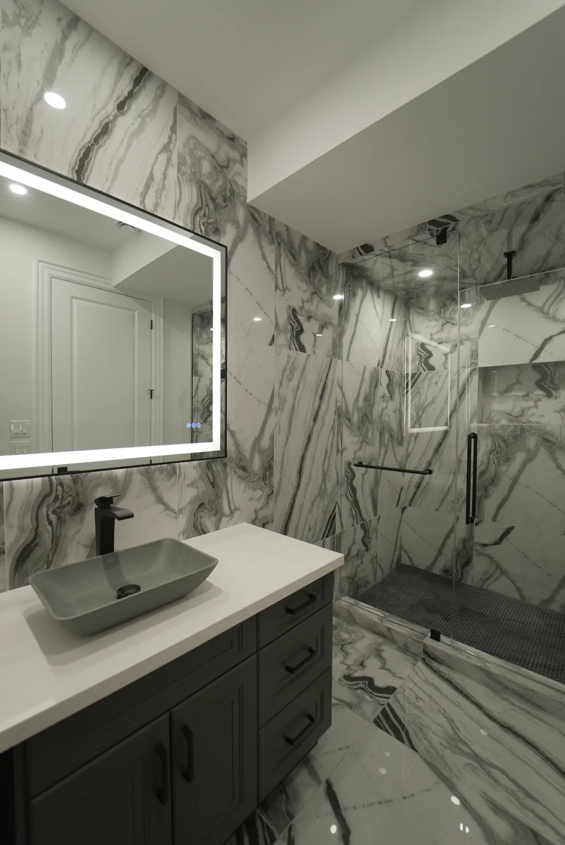 Bathroom with dark vanity, pale stone surfaces and a glass shower