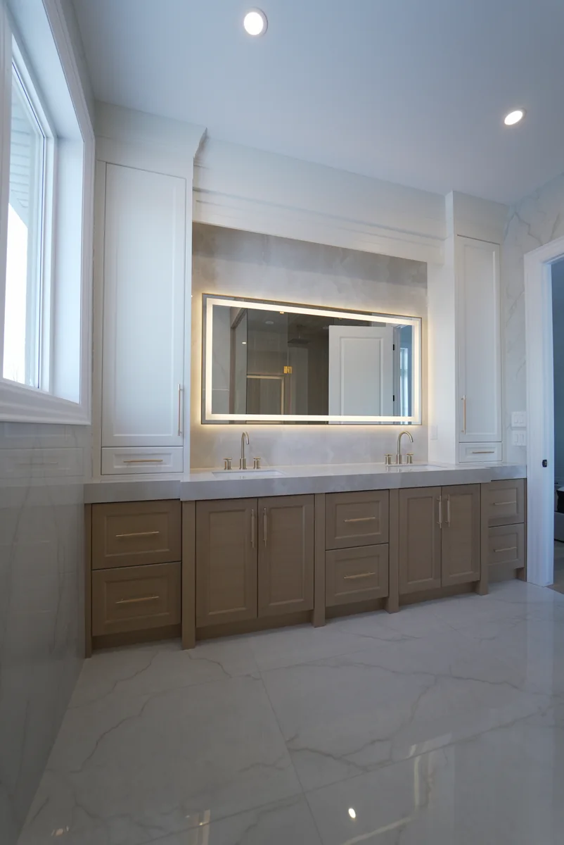 Front elevation of a double vanity with a pale stone counter and illuminated mirror